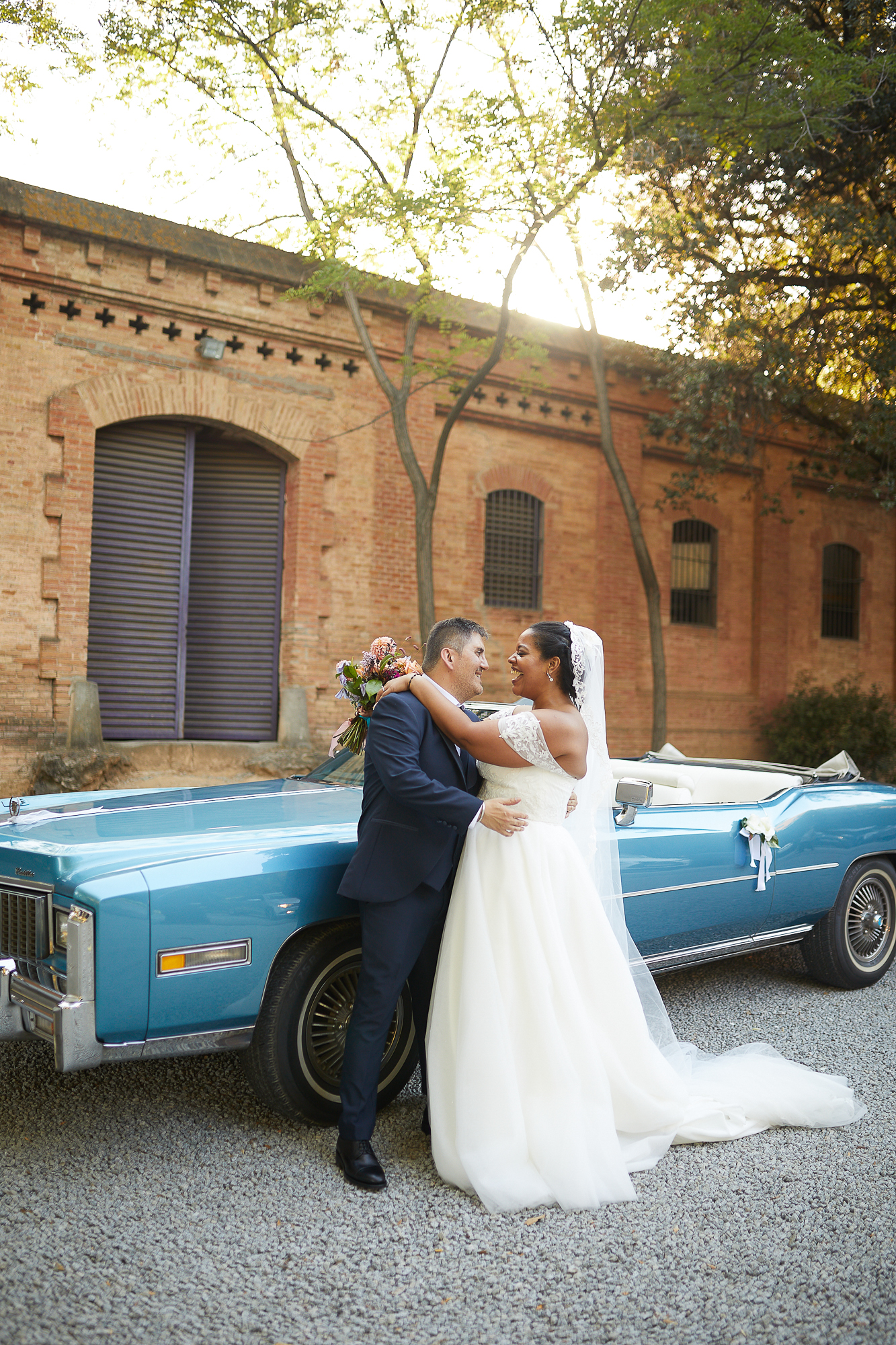 novios riéndose junto al coche después de la boda
